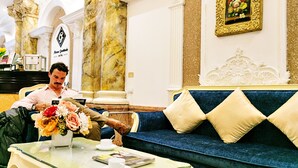 Ein Mann sitzt auf einem blauen Sofa in der Hotelhalle, mit einer Marmorsäule und einem gerahmten Blumenbild an der Wand.