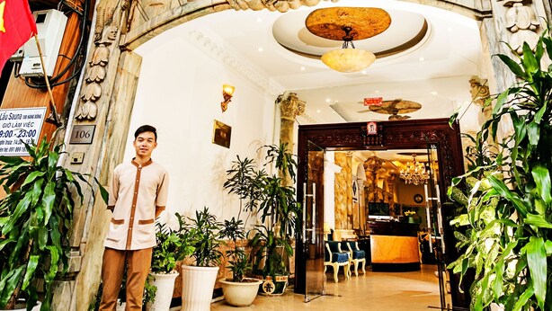Der Eingang zum Hanoi Gratuide Hotel mit aufwendigen architektonischen Details, einem Empfangsbereich und Topfpflanzen.