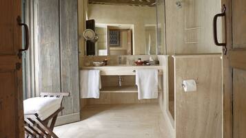 A bathroom with a wooden floor, a large mirror, and a sink with a towel hanging on the wall.
