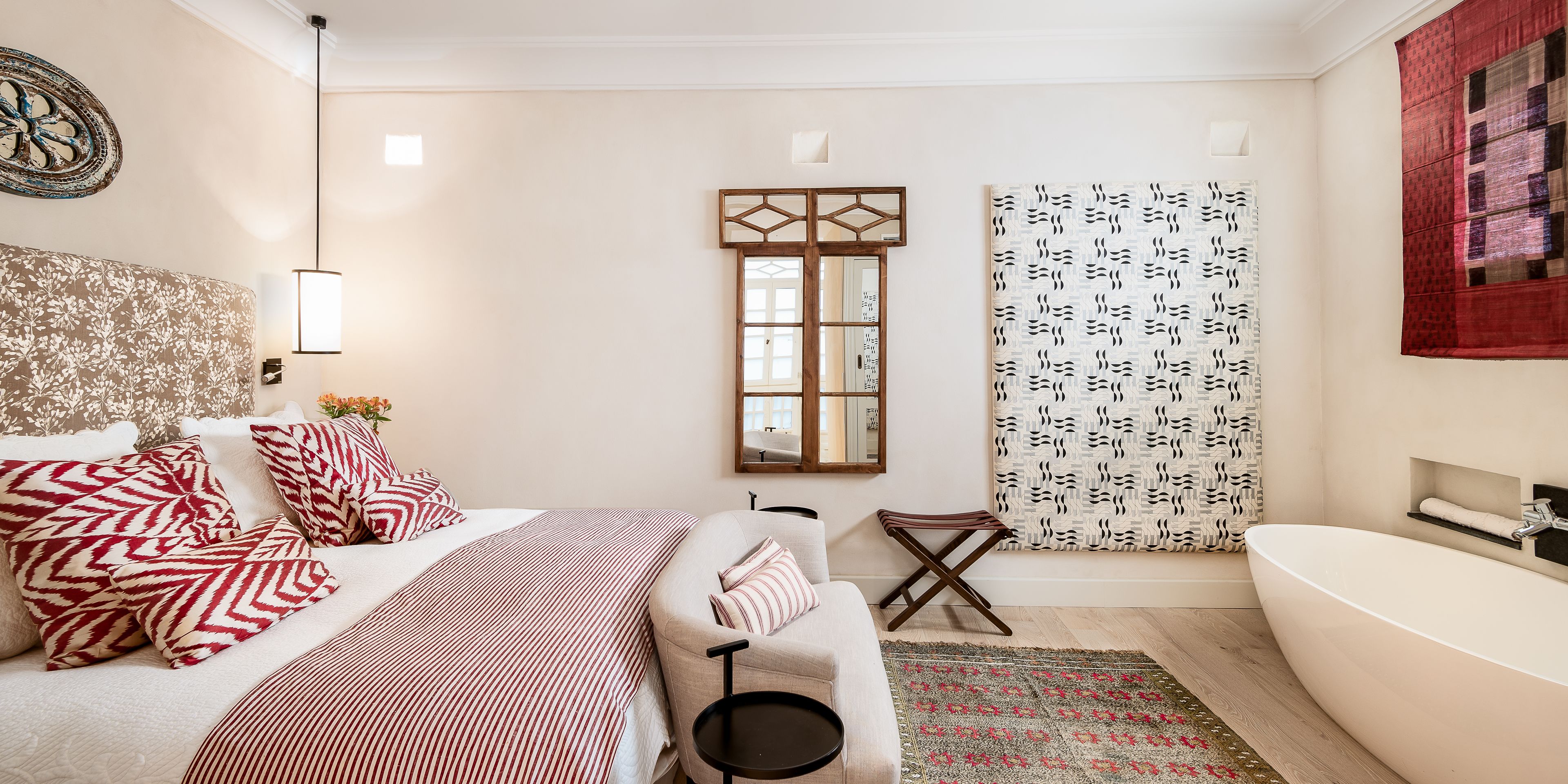 Une chambre moderne avec un grand lit, une table de chevet, un petit tabouret, une fenêtre avec un miroir et une salle de bain avec une baignoire.