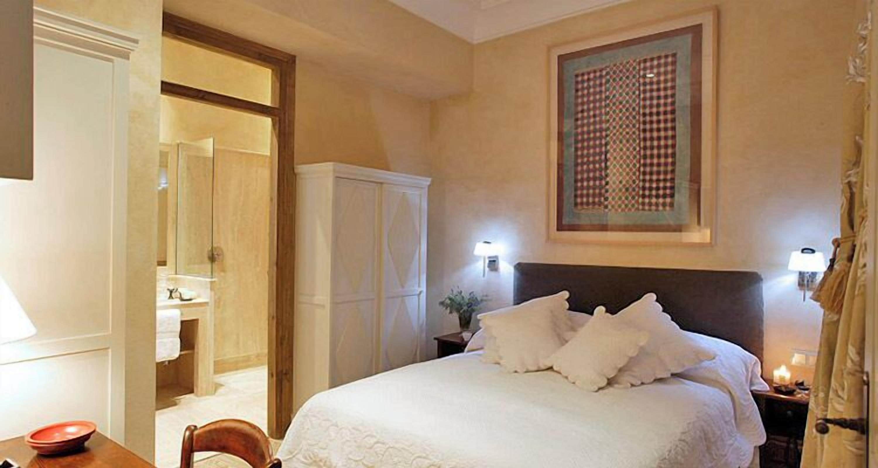 Une chambre d’hôtel comprenant un lit, une table de chevet, une lampe, une fenêtre donnant sur un paysage agréable et une porte menant à la salle de bain.