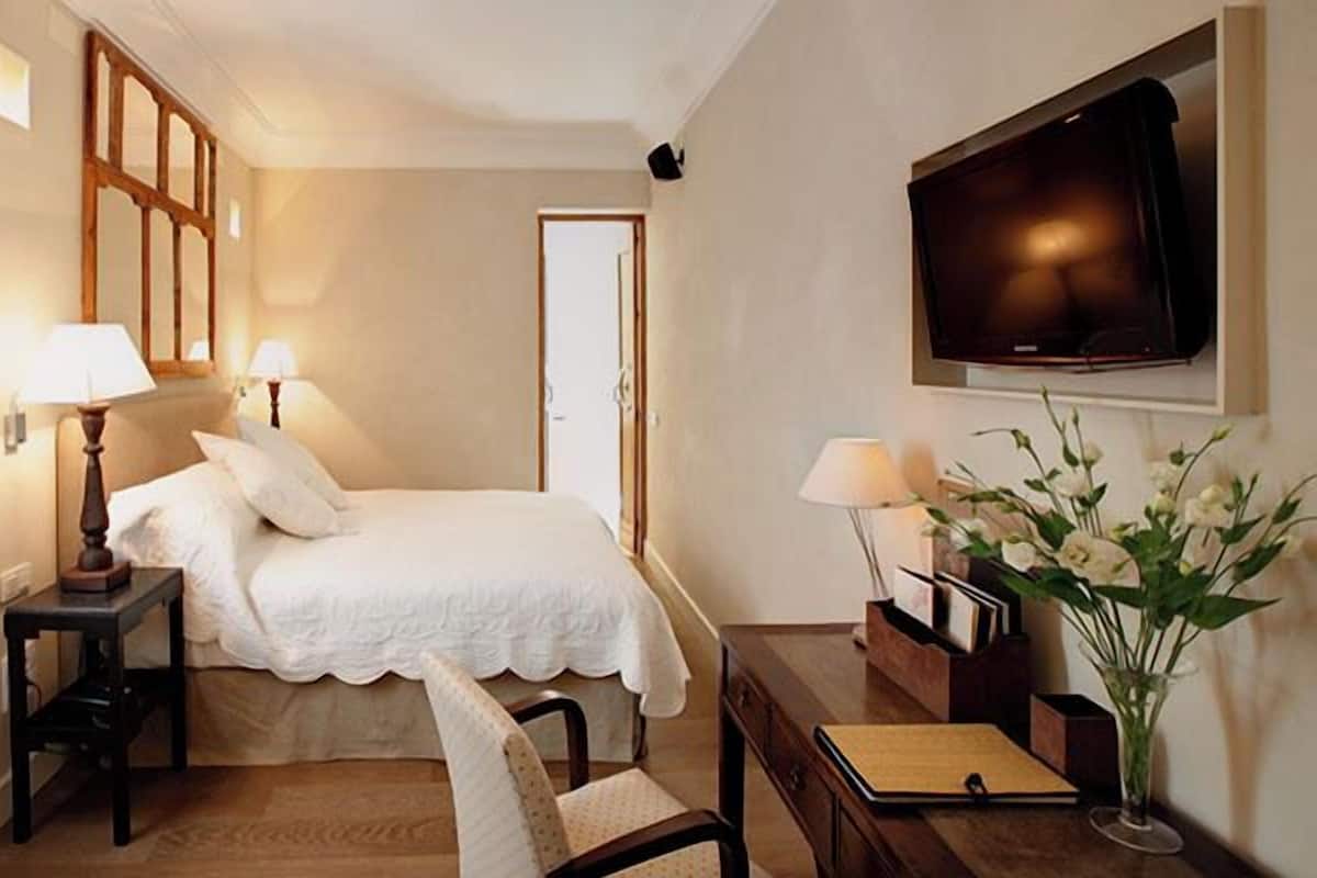 A hotel room with a bed, bedside tables, a desk, a chair, a TV, and a window with curtains.