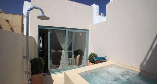 A modern outdoor bathroom with a shower, a small pool, and a glass door leading to a room.