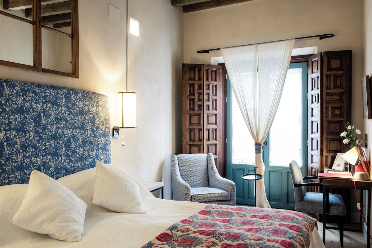 A bedroom with a bed, a chair, a desk, and a window with curtains.