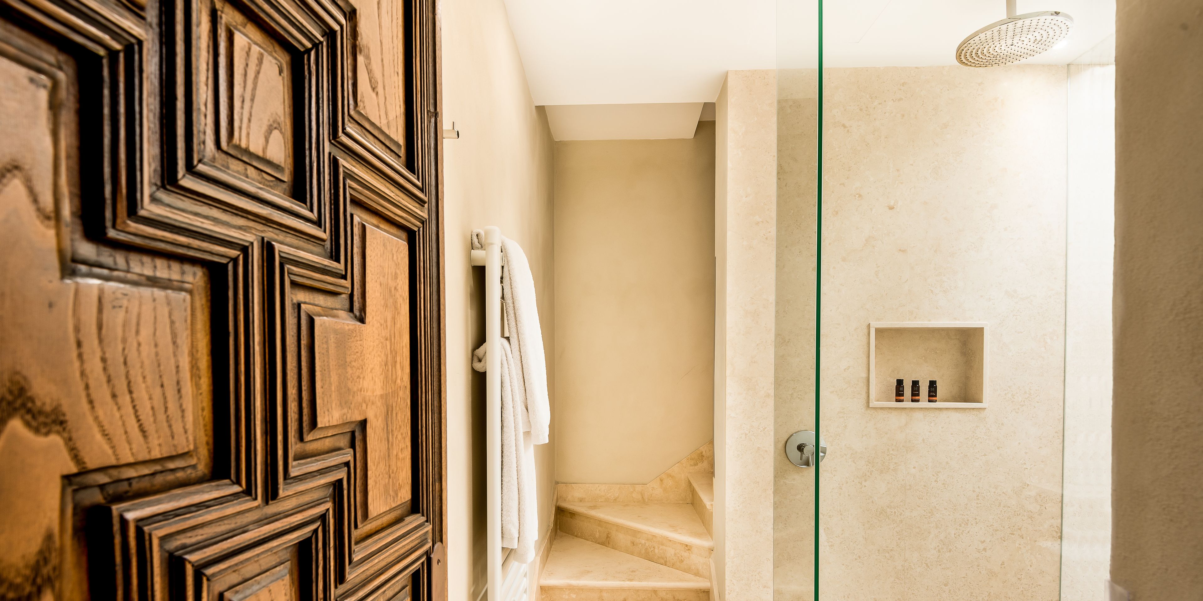 Un baño con puerta de madera, un perchero, zona de ducha y estante con artículos de aseo.