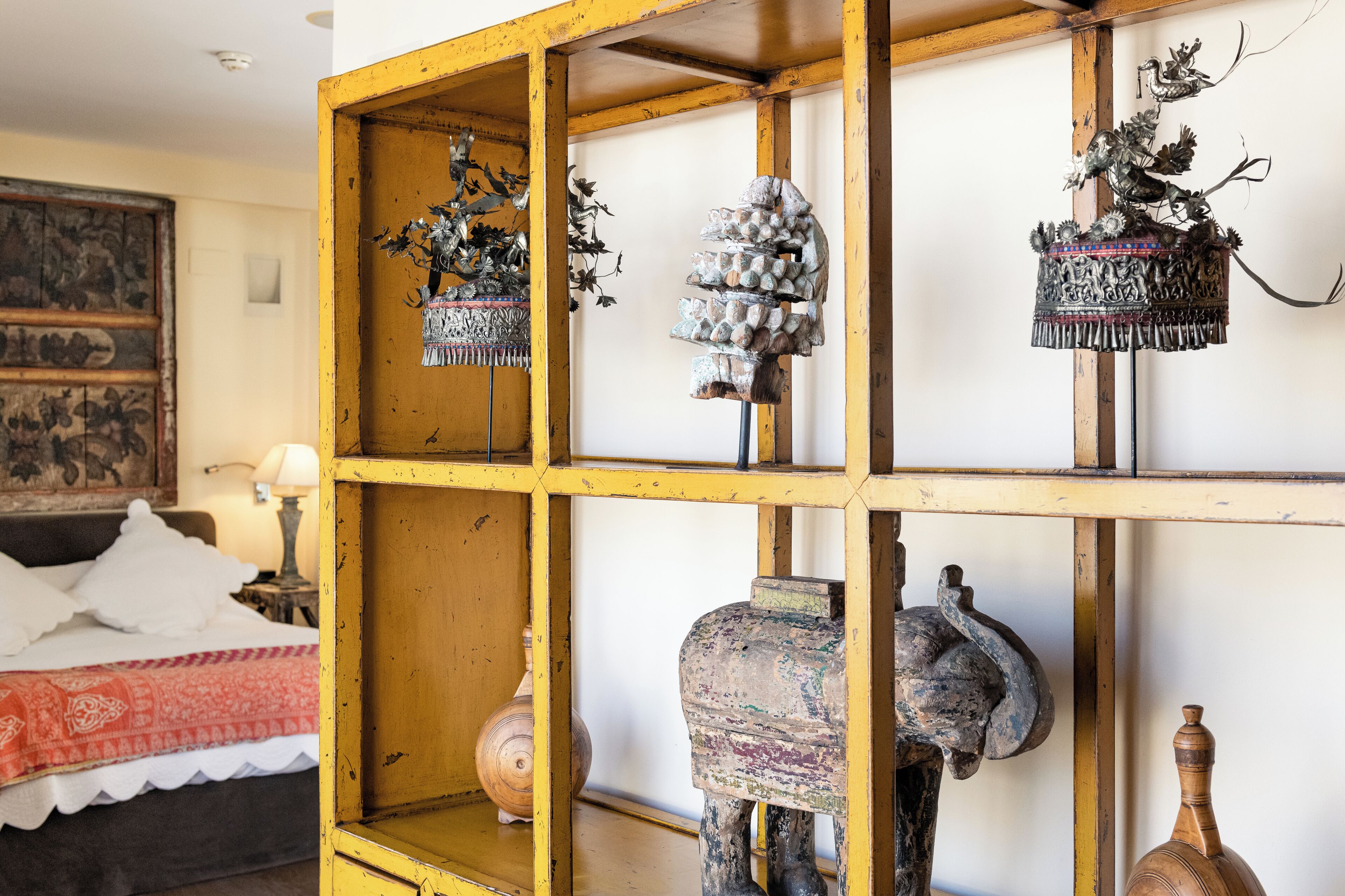 Une pièce comprenant un lit, une étagère en bois ornée d’objets décoratifs et un mur sur lequel est accroché un tableau.