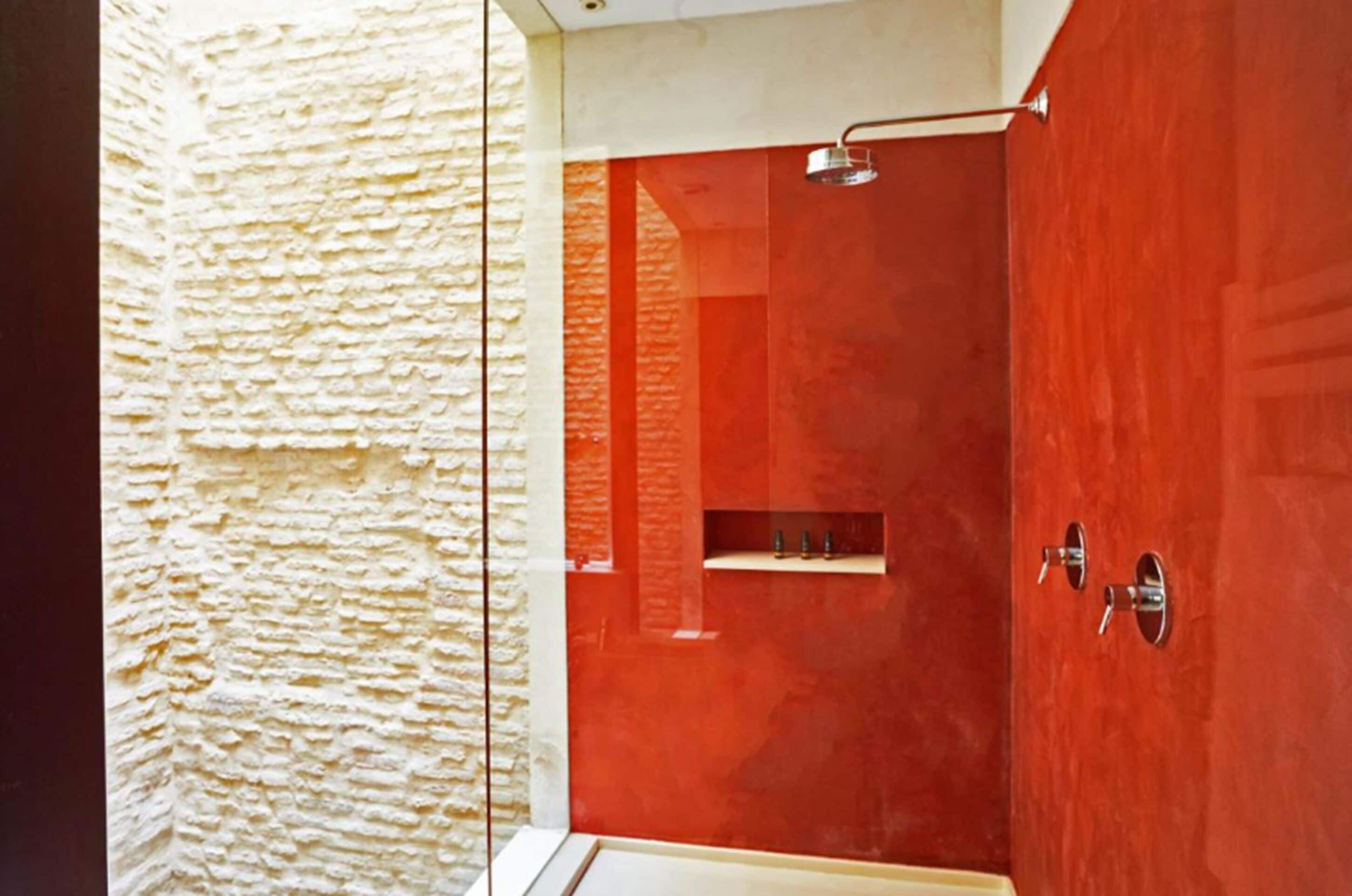 A bathroom with a textured wall, a red door, and a shower area.