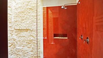A bathroom with a textured wall, a red door, and a shower area.
