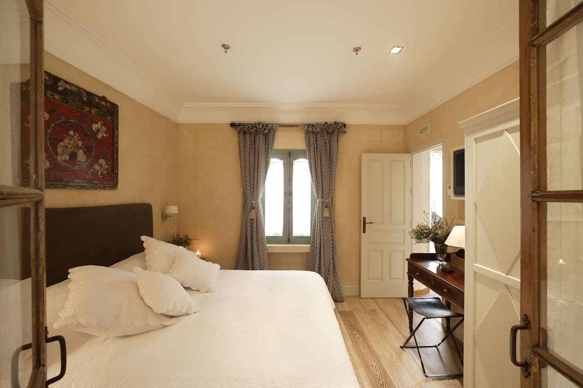 A bedroom with a large bed, a desk, and a window with curtains.