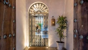 A stone-floored entrance with a wrought iron gate, a hanging light fixture, and a potted plant.