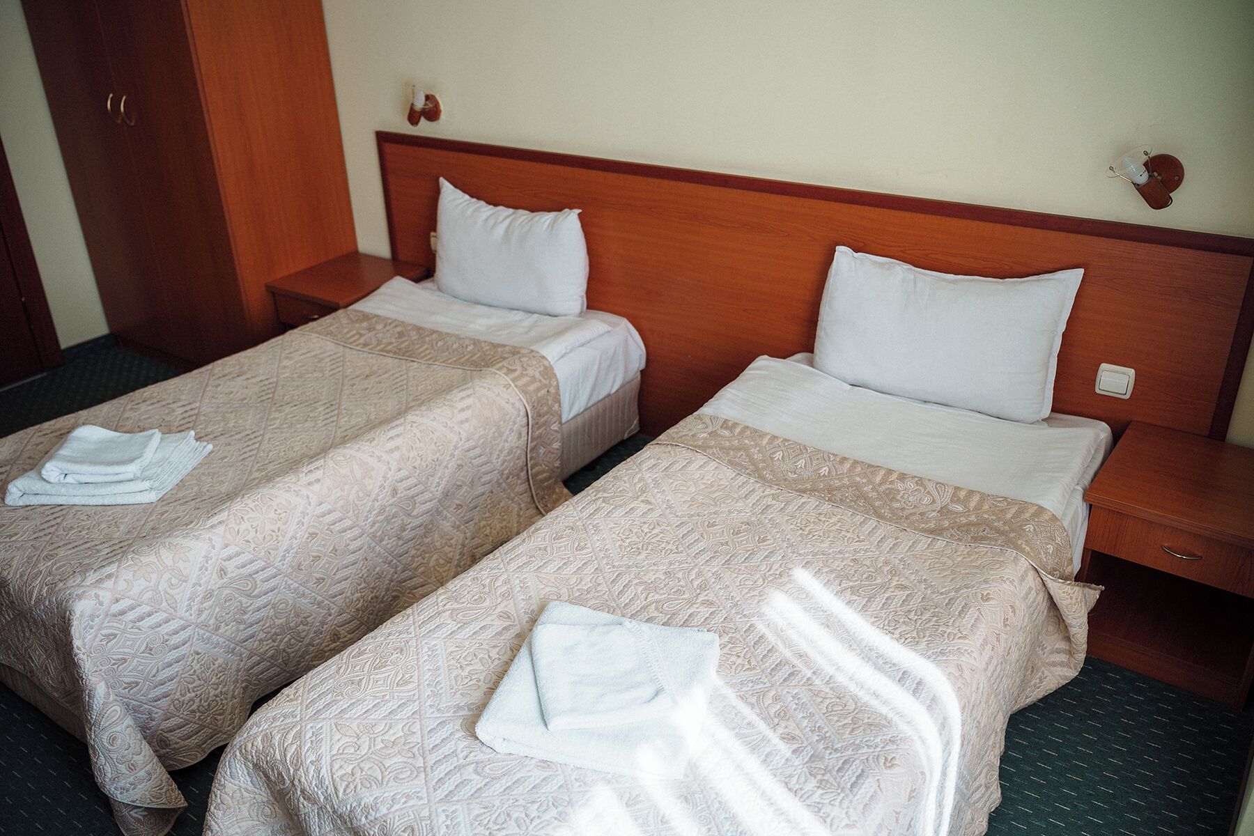 Two single beds with wooden headboards, white linens, and folded towels on the beds.