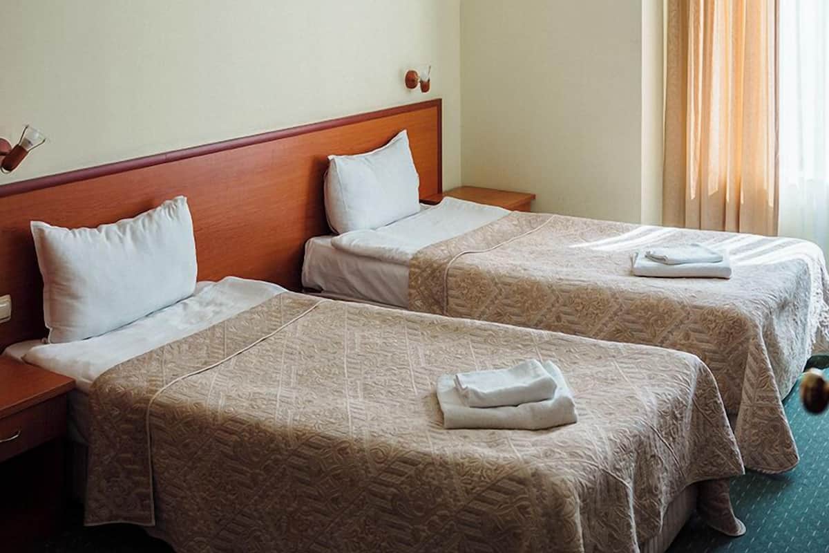A hotel room with two beds, a wooden headboard, a nightstand, and a window with curtains.