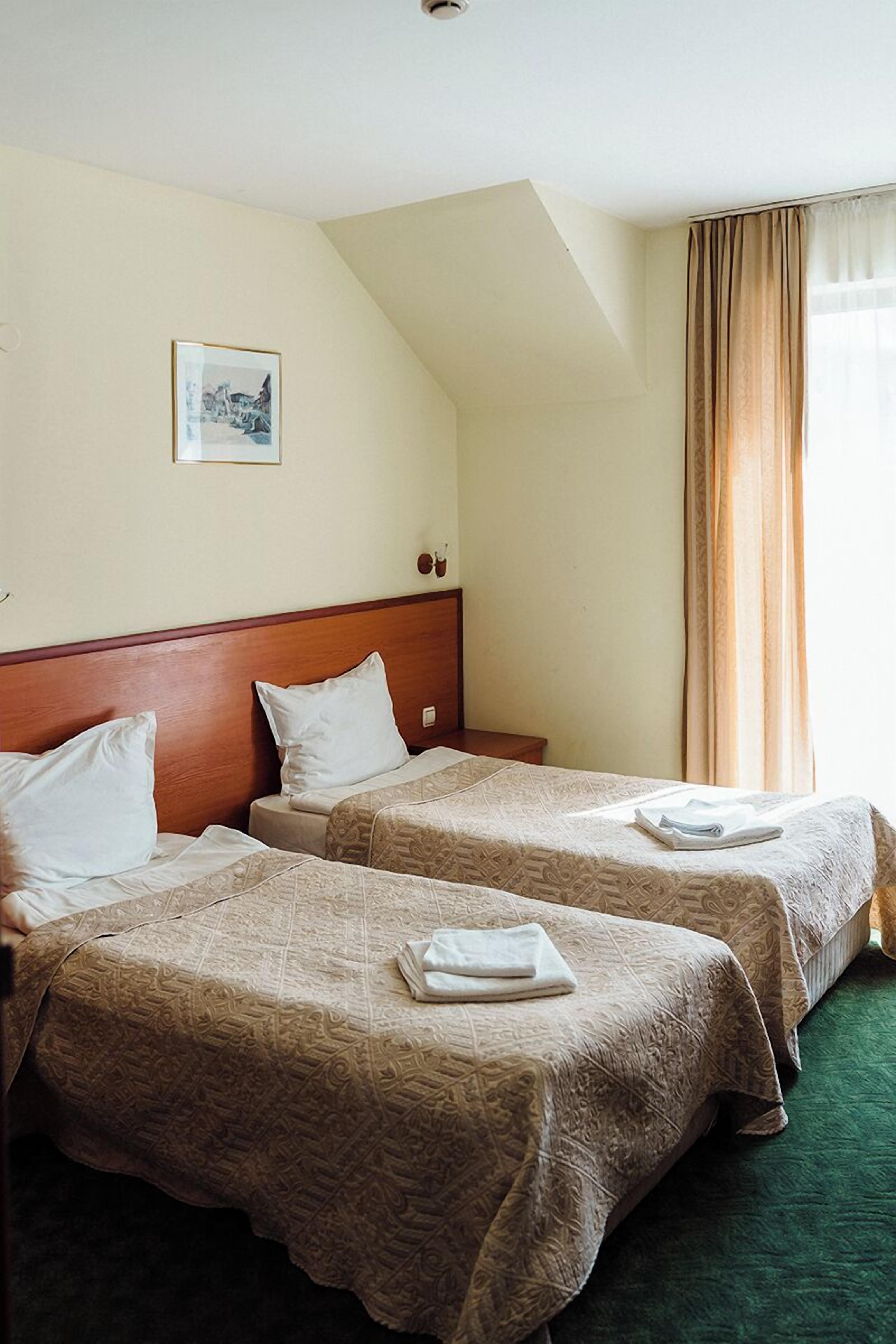 A hotel room with two beds, a wooden headboard, a framed picture on the wall, and a window with curtains.