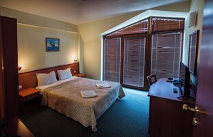 Habitación de hotel con cama, escritorio y un ventanal con persianas.