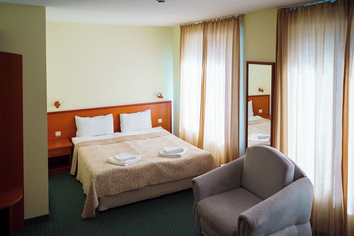 A hotel room with a bed, a chair, a nightstand, and a mirror.