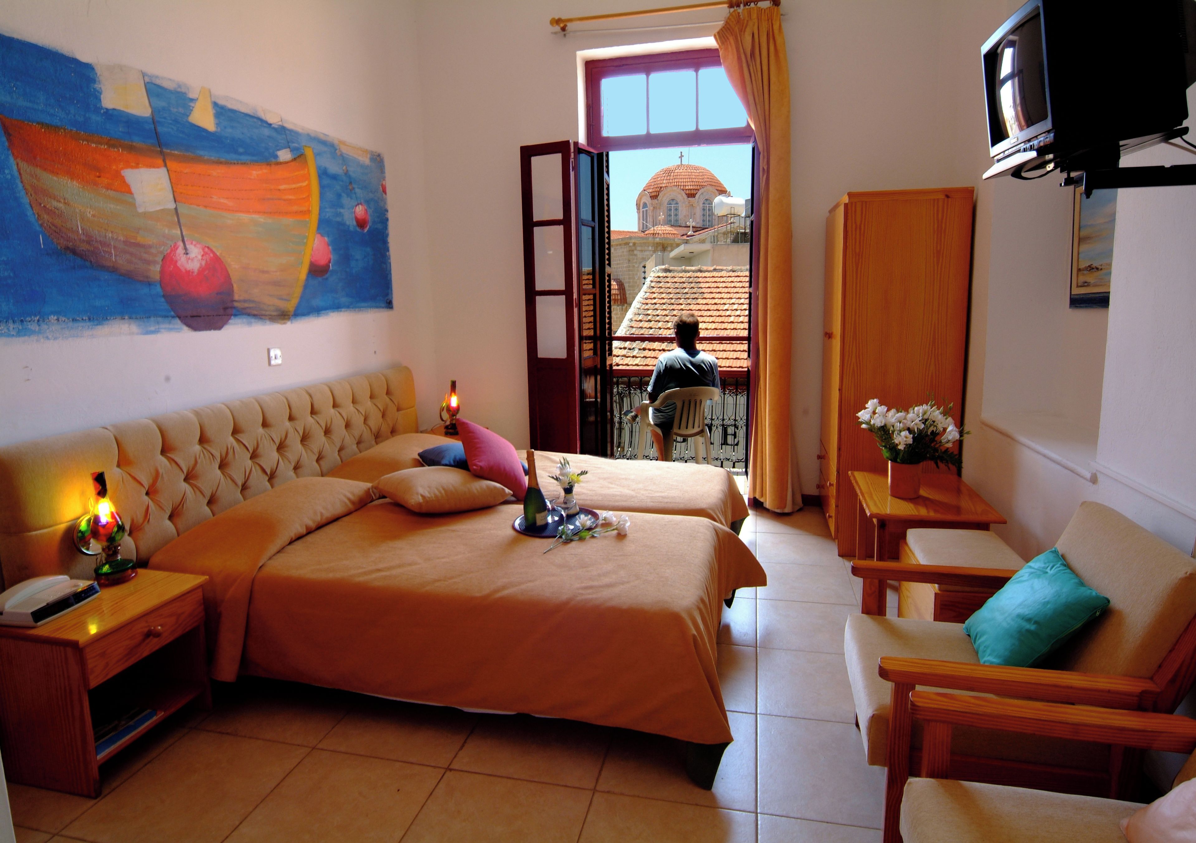 A room with two beds, a television, a painting, and a view of a building through a window.