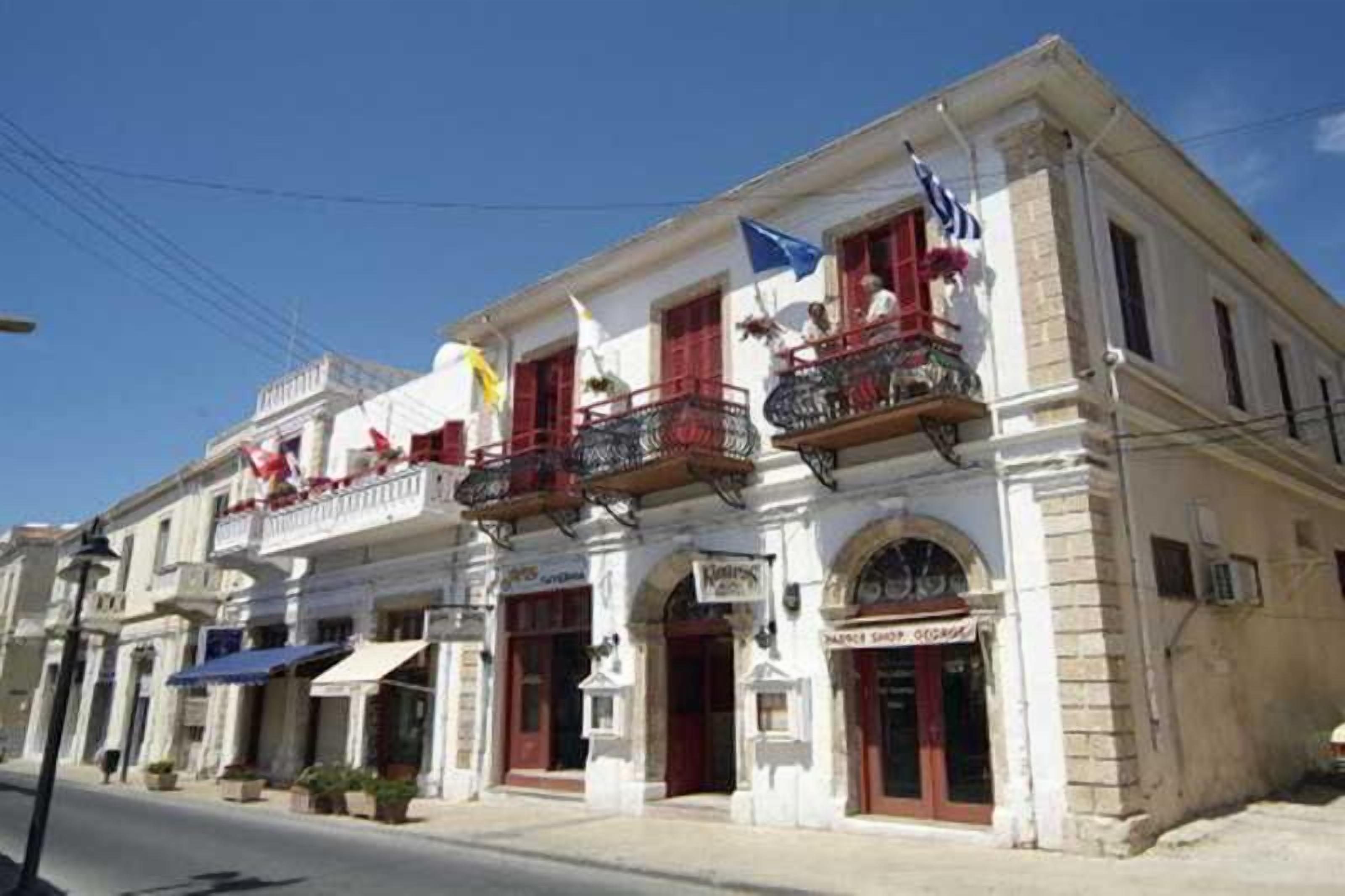 A two-story building with balconies, a shop on the ground floor, and flags.