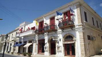 A two-story building with balconies, a shop on the ground floor, and flags.