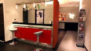 A bar area with a red counter, two stools, and a shelf with bottles. - Miramonti (Potenza)