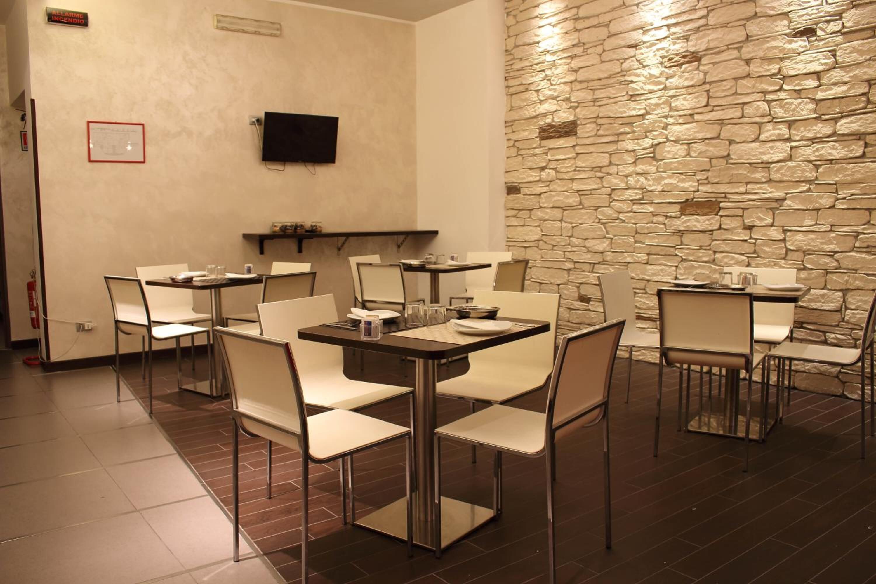 A dining area with multiple tables and chairs, a stone wall, a mounted television, and a fire extinguisher.