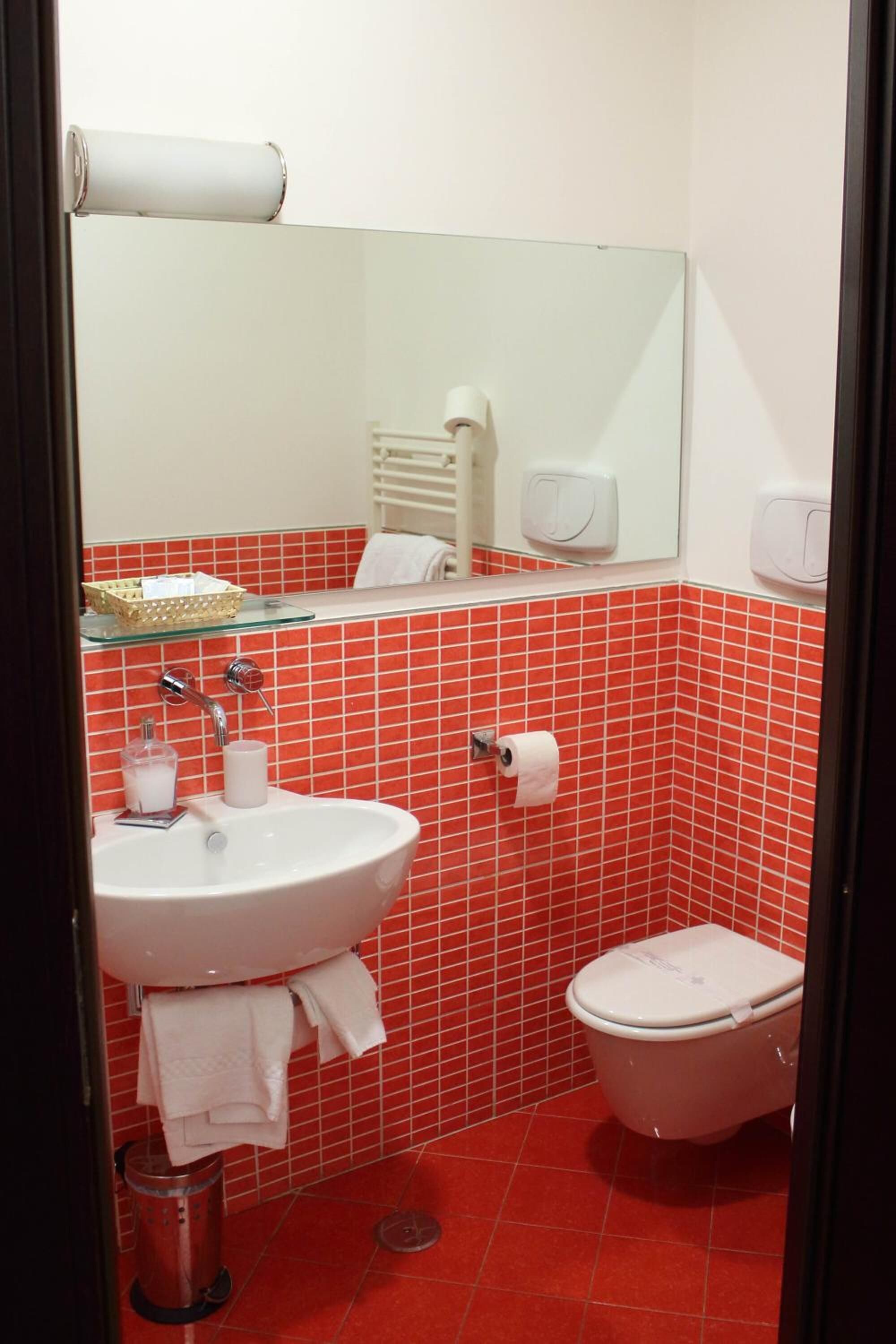 Un baño con lavamanos blanco, inodoro y paredes con baldosas rojas.