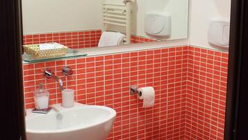 Un baño con lavamanos blanco, inodoro y paredes con baldosas rojas.