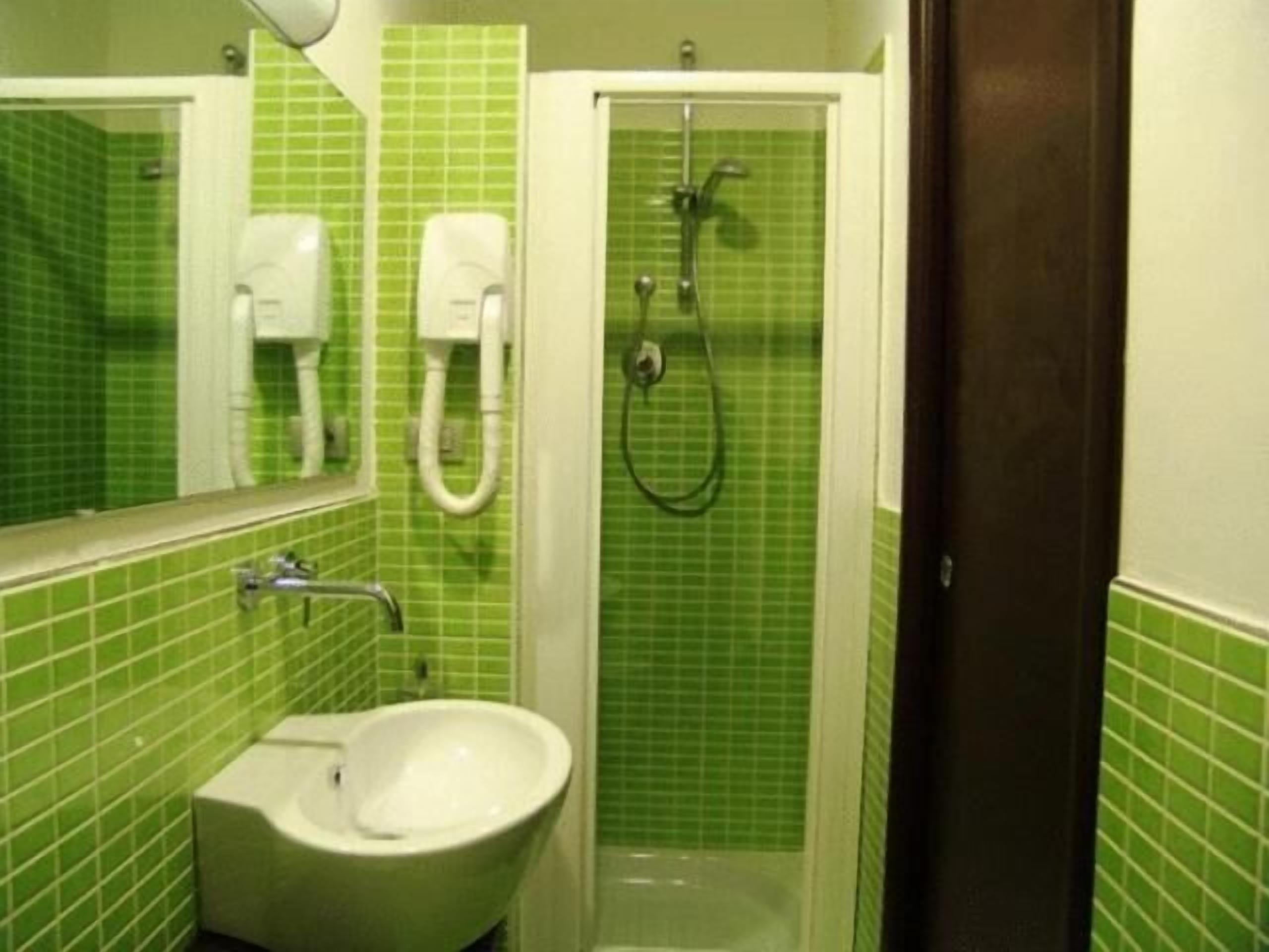 Un bagno con una parete rivestita di piastrelle verdi, un lavandino bianco, uno specchio e una doccia con soffione manuale.