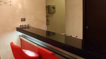Un espace bar avec un comptoir rouge, deux tabourets de bar rouges et des lampes suspendues.