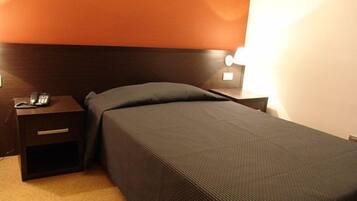 Ein Einzelbett mit dunklem Kopfteil in einem Hotelzimmer.
