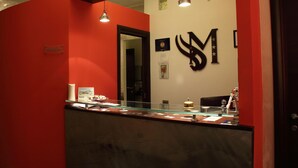 A reception area with a red wall, a glass counter, and a large black logo on the wall. - Miramonti (Potenza)