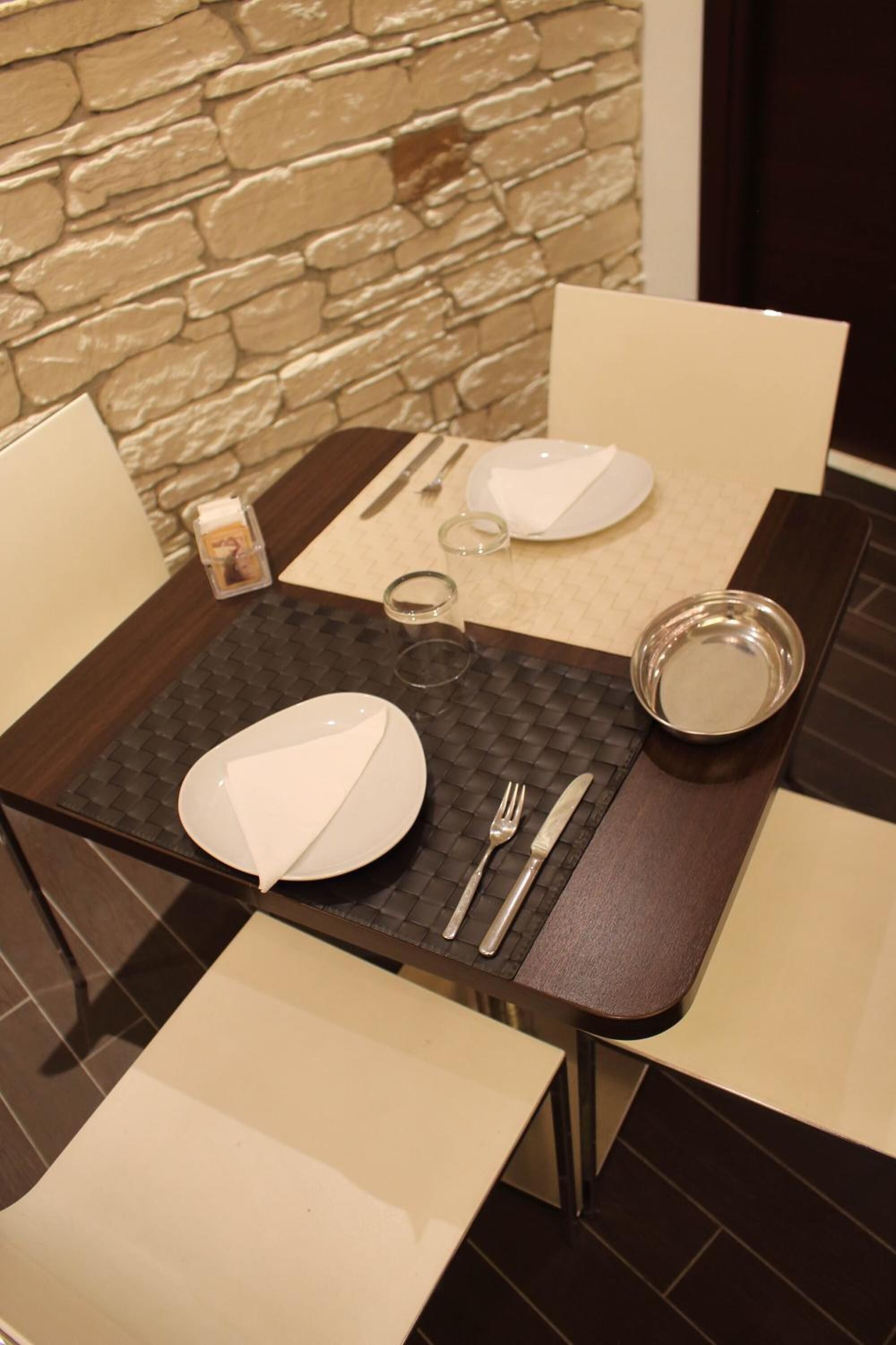 A dining table set with plates, cutlery, and glasses, with a stone wall in the background.