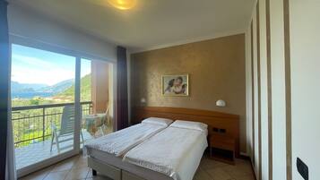 A hotel room with a bed, a balcony with a table and chairs, a painting on the wall, and a view of the landscape.
