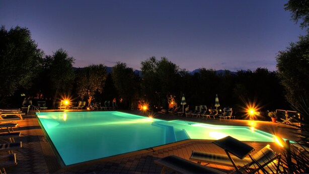 A swimming pool with lounge chairs and lights at night. - Casa Chincarini (Malcesine)