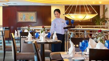 Une salle à manger bien éclairée, avec des tables dressées pour le service, un serveur s’occupant d’une table et un grand lustre au-dessus.