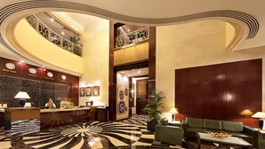 Eine Lobby mit einer Rezeption, einem Check-in-Schalter, einem grünen Sofa, einem Couchtisch und einer großen Wanddekoration.
