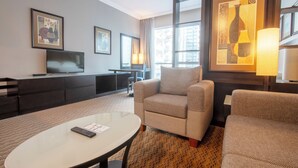 Ein Hotelzimmer mit Sofa, Sessel, Fernseher und Kunstwerken an den Wänden.