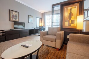 Una habitación de hotel con sofá, sillón, televisión y obras de arte en las paredes.