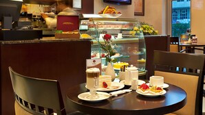 Ein Essbereich mit einem runden Tisch, gedeckt für zwei Personen, mit einer Desserttellere mit Kuchen und einem Glas mit einem schichtartigen Getränk.
