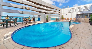 Una piscina en la azotea con vistas despejadas del horizonte urbano, rodeada de sillones de descanso y una zona de bar.