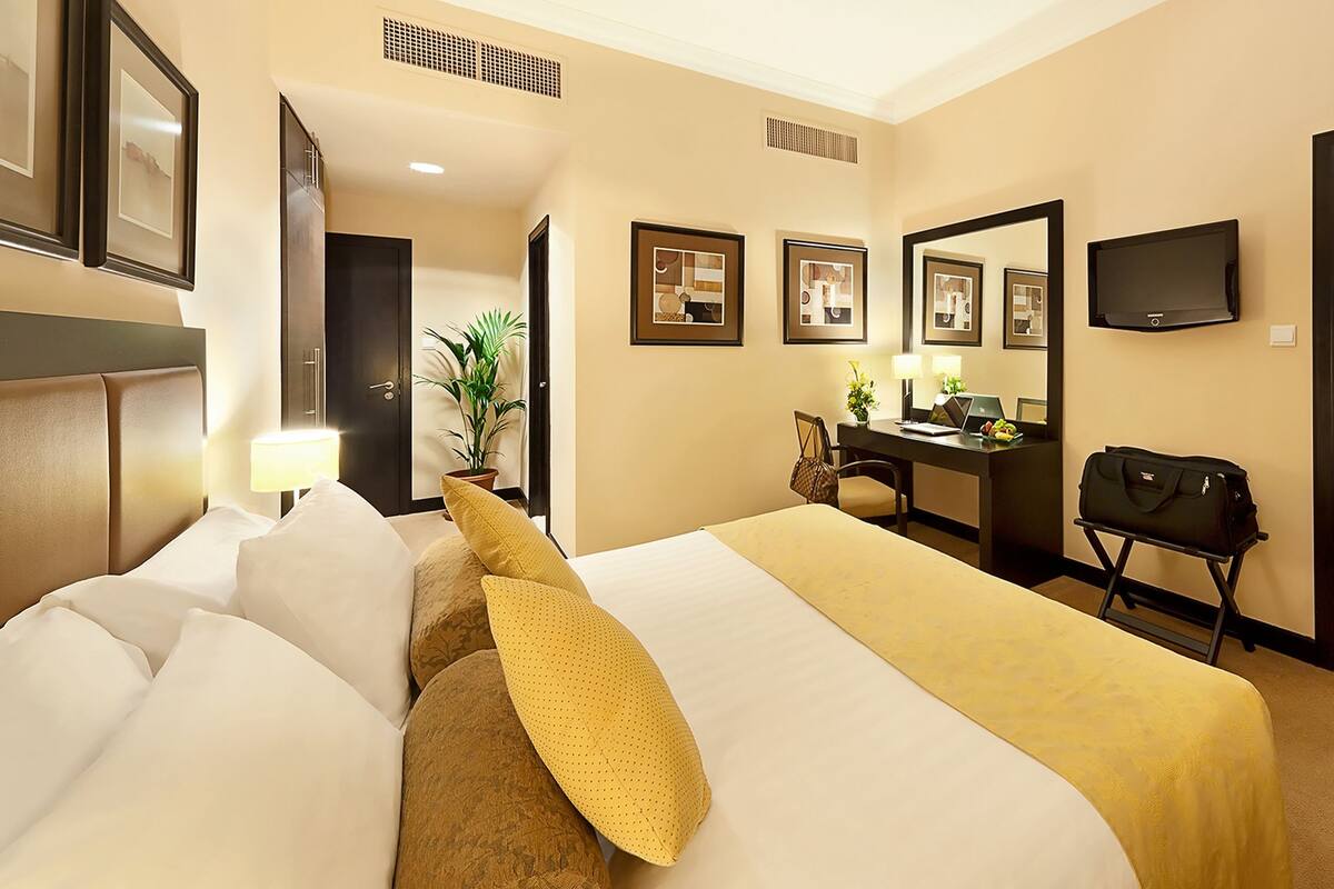 Habitación de hotel con cama, escritorio, silla, televisor y puerta que da a otra habitación.