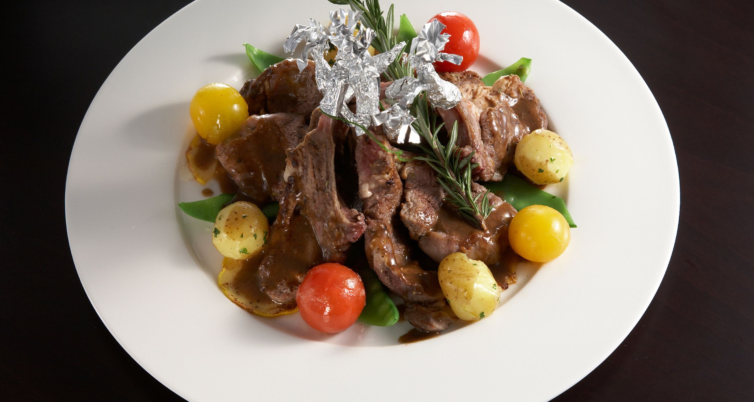 Un plato de comida con carne, papas y tomates cherry.