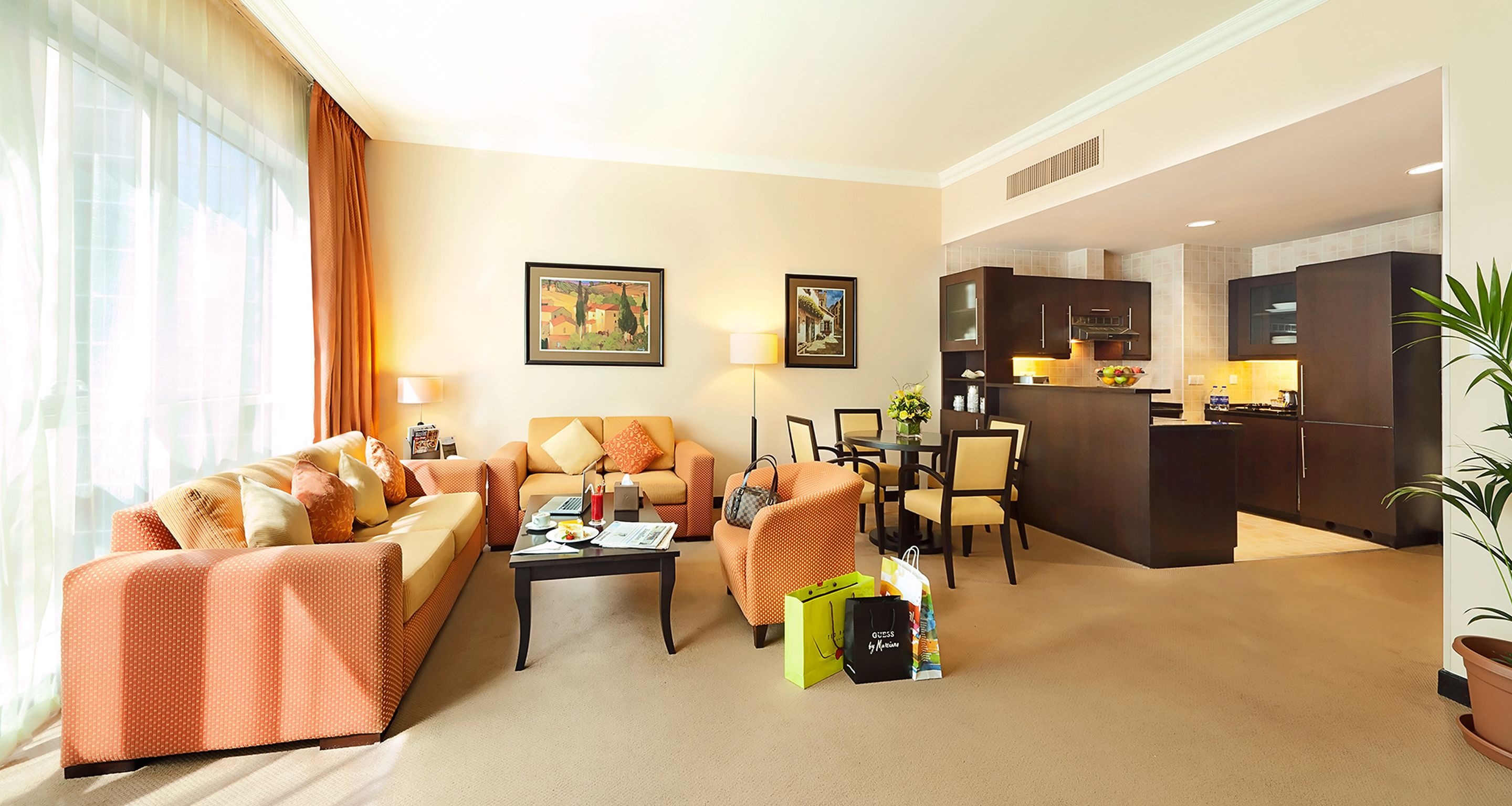 A hotel room with a living area, dining table, and kitchenette.