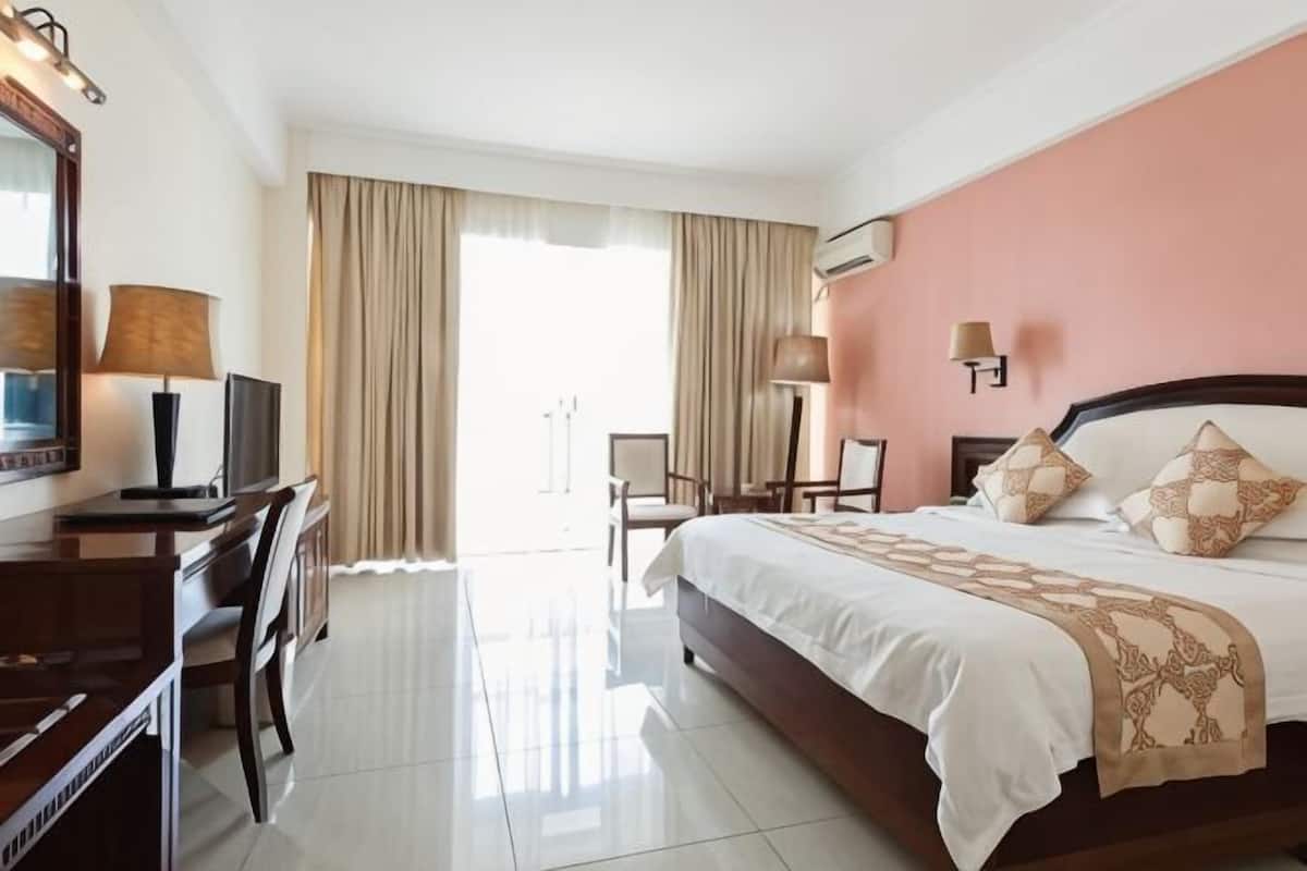 Quarto de hotel com cama, escrivaninha, cadeira, televisão e janela com cortinas.