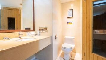 A bathroom with a wooden door, a toilet, a sink with a mirror, and a framed picture on the wall.