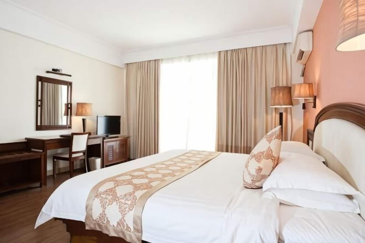 Quarto de hotel com cama, escrivaninha, cadeira, televisão e cortinas.