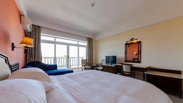 A hotel room with a large bed, a desk, a chair, a television, and a balcony with a view. - Lihua Hotel Haikou (Haikou)