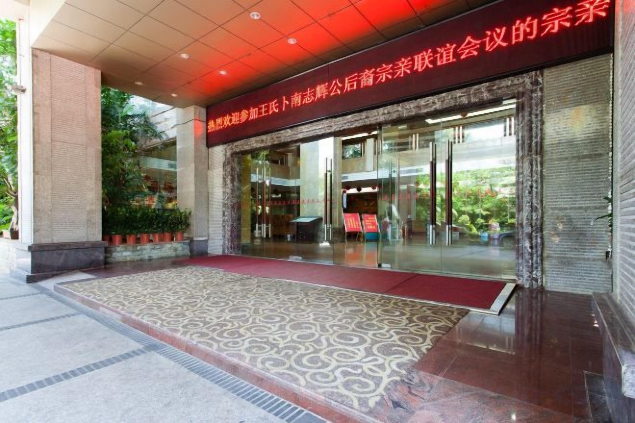 A hotel entrance with a red carpet, glass doors, and a red banner above.