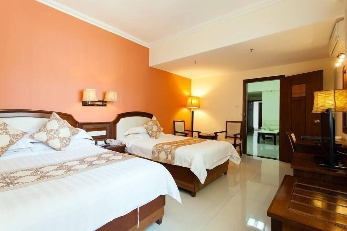 Quarto de hotel com duas camas, uma escrivaninha, uma cadeira, um abajur e uma televisão.