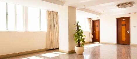 A hotel corridor with a potted plant, a door with a sign, and a window with curtains.