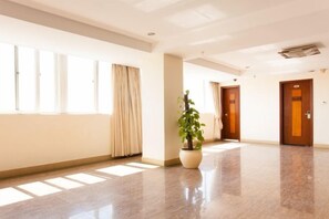 A hotel corridor with a potted plant, a door with a sign, and a window with curtains.